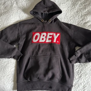 Svart hoodie från Obey - Säljer en svart hoodie från Obey med stor röd och vit logga på bröstet. 