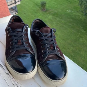 Lanvin vinröda - Snygga vinröda sneakers från Lanvin med svarta snören och en glansig svart tå. Skorna är lite slitna därför priset, ganska ovanliga och väldigt snygga. Ser lite bruna ut på bilderna men de är vinröda. 