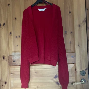 Röd stickad kofta - Säljer en mysig röd stickad kofta med långa ärmar. Perfekt för kyliga dagar och enkel att matcha med olika outfits. Koftan har en öppen design utan knappar.