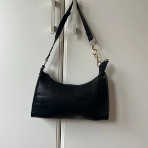 Svart axelväska med krokodilmönster - svart axelväska med krokodilmönster bandet är sliten.