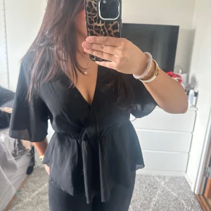 Svart blus men volang - Snygg svart blus med volang och resårband i midjan och korta ärmar. Perfekt för en stilren look.