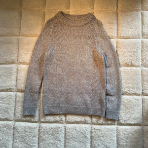 Grå stickad tröja - Säljer en mysig grå stickad tröja med rund hals och långa ärmar. Perfekt för kyliga dagar. Tröjan är tillverkad av en blandning av material som ger både värme och komfort. Passar bra till våren. storlek M passar även L