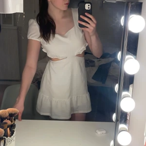 Vit kortklänning med volangdetaljer - Säljer en söt vit kortklänning med volangdetaljer och öppen och en fin skärning i midjan.