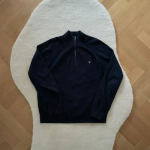 Mörkblå tröja med dragkedja från GANT 152 - Snygg mörkblå tröja från GANT med halv dragkedja framtill. Perfekt för kyligare dagar med sin stilrena design och bekväma passform. Tröjan har långa ärmar och är tillverkad i ett mjukt material. Storleken är 12 år/ storlek 152. 