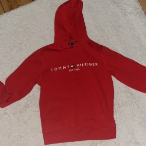 Röd hoodie från Tommy Hilfiger - Säljer en snygg röd hoodie från Tommy Hilfiger med deras ikoniska logga på bröstet. Perfekt för en avslappnad stil. Den har en klassisk huva och långa ärmar.