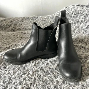 Svarta korta boots - Snygga svarta boots med elastiska paneler på sidorna för enkel på- och avtagning. Perfekta för både höst och vinter med en stilren design som passar till det mesta. Knappt använda, endast ett fåtal gånger.