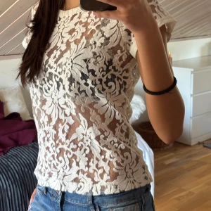 Vit spetsblus - Säljer en elegant vit spetsblus med korta ärmar. Blusen har ett vackert blommigt mönster och är perfekt för en stilren look. Passar bra till jeans eller kjol för en chic outfit.