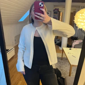 Vit stickad kofta - Säljer en stilren vit stickad kofta med en knapp vid halsen och långa ärmar. Perfekt för en avslappnad look. Koftan har en enkel design utan mönster och är lätt att matcha med olika outfits.