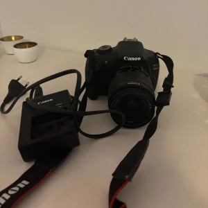 Canon EOS 1200D kamera med laddare - Säljer en Canon EOS 1200D digital systemkamera med tillhörande laddare. Perfekt för både nybörjare och entusiaster som vill ta högkvalitativa bilder. Kameran har en robust design och levereras med en praktisk rem för enkel hantering. Passa på att fånga dina bästa ögonblick med denna pålitliga kamera! 📷