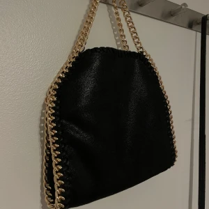 Svart väska med guld detaljer - Super fin väska med guld kedjor. Väskan är aldrig använd alltså är den i väldigt bra skick. Måtten ser du på sista bilderna.