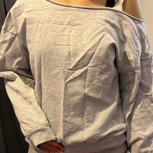 Grå offshoulder tröja - Säljer en stilren grå offshoulder tröja med långa ärmar. Perfekt för en avslappnad look. Tröjan har en bekväm passform och ribbade muddar vid ärmslut och nederkant.