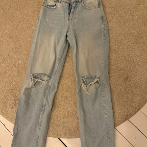 Ljusblå jeans med hål  - Säljer ett par ljusblå jeans från Gina tricot med coola slitna detaljer på knäna. De har en klassisk femficksdesign och dragkedja med knapp framtill.  Hålet på höger knä är lite spräckt (se bild) innerbenslängd 78cm, tvärs över midjan 35cm