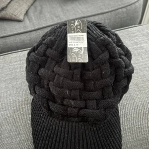 Svart stickad mössa - Snygg svart stickad mössa med ett unikt flätat mönster. Perfekt för att hålla värmen under kyliga dagar. Tillverkad av 100% akryl.