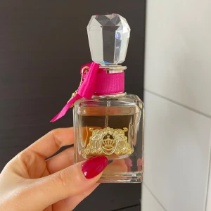 Viva La Juicy Parfym från Juicy Couture - Säljer en lyxig Viva La Juicy parfym från Juicy Couture. Flaskan har en elegant design med en stor, kristalliknande kork och en rosa rosett. Förpackningen är i en livlig rosa färg med gyllene detaljer. Perfekt för den som älskar en söt och fruktig doft.