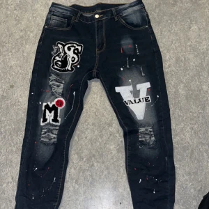 Svarta Dsquard2 jeans med patchar - Coola svarta jeans med unika patchar och slitna detaljer. Byxorna har en normal passform och är dekorerade med olika mönster och text. Perfekta för en trendig look.