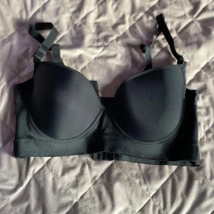 Svart bh som liknar en korsett - Snygg svart korsettliknande BH med justerbara axelband och vadderade kupor för extra stöd. Perfekt för att skapa en stilren och elegant look. Toppen har en slät yta och en bekväm passform. Extra mycket spännen i back för bra och bekvämt stöd!  Storlek 100F/44 Knappt använd! Öppen för prisförslag 