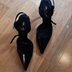 Svarta pumps från Zara - Eleganta svarta pumps från Zara med spetsig tå och smal klack. Skorna har en stilren design med justerbara remmar för en perfekt passform. Perfekta för en chic och sofistikerad look.