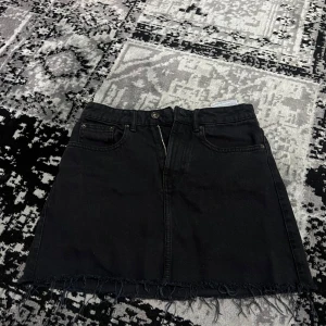 Svart jeanskjol från TRF - Snygg svart jeanskjol från TRF med rå kant och klassisk femficksdesign. Perfekt för en avslappnad stil. 