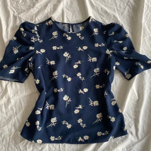 Blommig blus i mörkblått - Aldrig använt av mig då jag fick den av en vän. Pyttesmå defekter, men ingenting man märken när man har på sig den. Står inte storlek, men jag antar att det passar folk med M eller S 