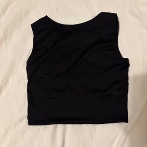 Svart ärmlös topp - Snygg svart ärmlös topp i ett mjukt och stretchigt material. Perfekt för en stilren look. Toppen har en enkel design som gör den lätt att matcha med olika outfits.