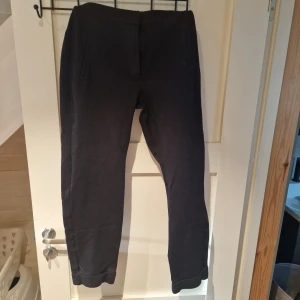 Svarta byxor från Lindex - Säljer ett par svarta byxor i kostymbyxstil från Lindex i storlek 38. Byxorna har en tight passform och är tillverkade i ett mjukt material. Perfekta för en stilren look.