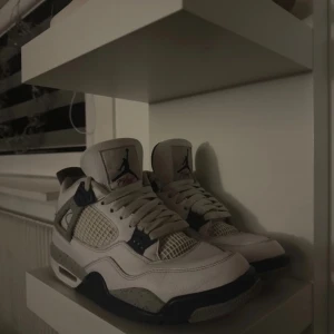 jordan 4 - Snygga Nike Air Jordans i vit och beige med mörka detaljer. Skorna har en klassisk design med snörning och en bekväm passform. Perfekta för dig som vill ha stil och komfort i ett.