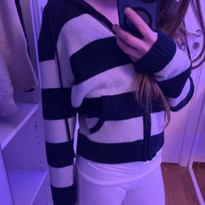 Randig hoodie från Brandy Melville - Säljer en mysig randig hoodie från Brandy Melville i svart och vit. Tröjan har en dragkedja framtill och en luva, perfekt för en avslappnad stil. Den är stickad och har långa ärmar.