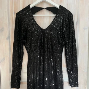 Svart glittrig klänning - Snygg svart klänning med glittriga paljetter och v-ringning. Den har långa ärmar och en elegant passform som passar perfekt för festliga tillfällen. Klänningen har en stilren design med en öppen rygg som ger en extra touch av glamour.💞