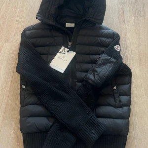 Moncler Cardigan  - Säljer min Moncler Cardigan i nyskick. Jackan är använd ett fåtal gånger och är i riktigt fint skick. Storlek M/L, passar båda. Den är svart och riktigt skön med huva! 10/10 skick! Lappar och påse fås med.