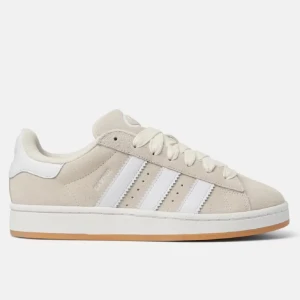 Beige sneakers från Adidas - Snygga beige sneakers från Adidas med klassiska vita ränder och en gummisula. Skorna har snörning och är tillverkade i mocka för en stilren look. Perfekta för en avslappnad stil.