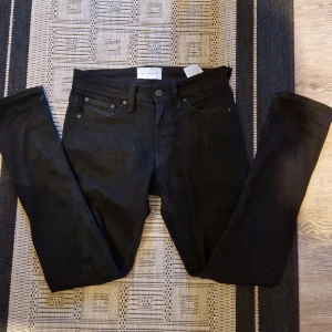 Svarta jeans från TeeShoppen - Snygga svarta jeans från TeeShoppen med en tight passform. Perfekta för en stilren look. De har en klassisk design med fem fickor och knappgylf.