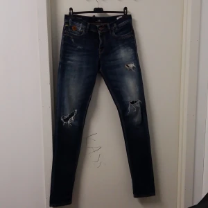 Blå jeans med slitningar från LTB - Snygga blå jeans från LTB med coola slitningar på framsidan. De har en skinny passform och är perfekta för en avslappnad stil. Klassisk femficksdesign och knappgylf.