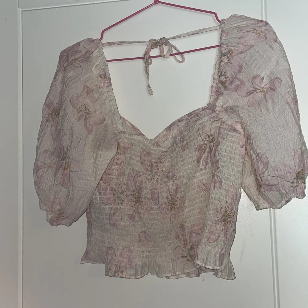 Säljer en söt blommig topp från H&M med puffiga ärmar och knytning i ryggen. Toppen har en v-ringad design och är dekorerad med ett vackert blommönster i rosa och beige nyanser. Perfekt för en somrig look! 🌸. Yläosat.
