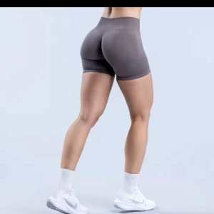 Grå träningsshorts från DFYNE - Snygga grå träningsshorts från DFYNE med hög midja och tight passform. Perfekta för gymmet eller löprundan. De är tillverkade i ett stretchigt syntetmaterial som ger bra rörelsefrihet. Logotypen är diskret placerad vid midjan.