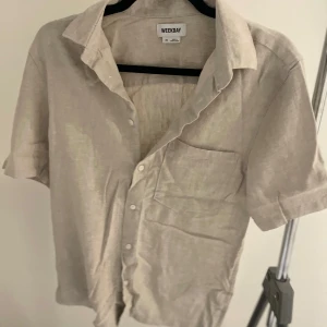 Beige kortärmad skjorta från Weekday - Säljer en stilren beige kortärmad skjorta från Weekday. Skjortan har en klassisk krage och knappar framtill. Perfekt för en avslappnad look. Den är i materialet linne! Har du några frågor så är de bara att höra av sig! Pris kan diskuteras vid en snabb affär!