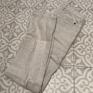 Beige linnebyxor från NN07 - Snygga beige linnebyxor från NN07 med dragkedja och knapp framtill. Perfekta för en stilren look med sin raka passform och midwaist-design. Byxorna har hällor för bälte och är tillverkade i ett lätt och luftigt material. Storlek: 31/34, nypris: 1300kr 