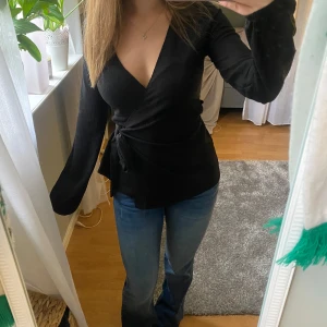 Svart omlottopp med knytband - Snygg svart omlottopp med v-ringning och knytband i midjan. Från Na-Kd och använd 1 gång 🫶
