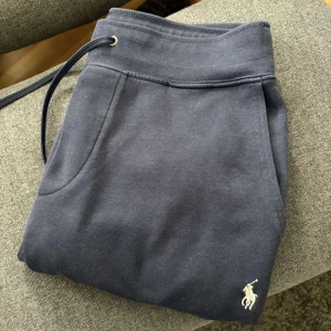 Mörkblå mjukisbyxor från Polo Ralph Lauren - Säljer ett par mörkblå mjukisbyxor från Polo Ralph Lauren med broderad logga. Byxorna har snörning i midjan och är tillverkade i mjukt bomullsmaterial. Perfekta för en avslappnad stil. Ny pris 1800kr. Skick ca 8/10 det som drar ner skicket är nopper men som är enkelt att ta bort. OBS! Pris kan diskuteras 