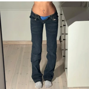 Lågmidjade Mörkblå jeans med dragkedjedetaljer - Snygga mörkblå jeans med låg midja och bootcut-stil. De har unika dragkedjor på bakfickorna. Bilderna är lånade från tjejen jag köpte dem av. Jag har sprättat upp dem där nere så att dem blev längre. I längden passar dem mig bra (referns ör jag 176 och jeansen är långa på mig) säljer pga att dem är för små i midjan