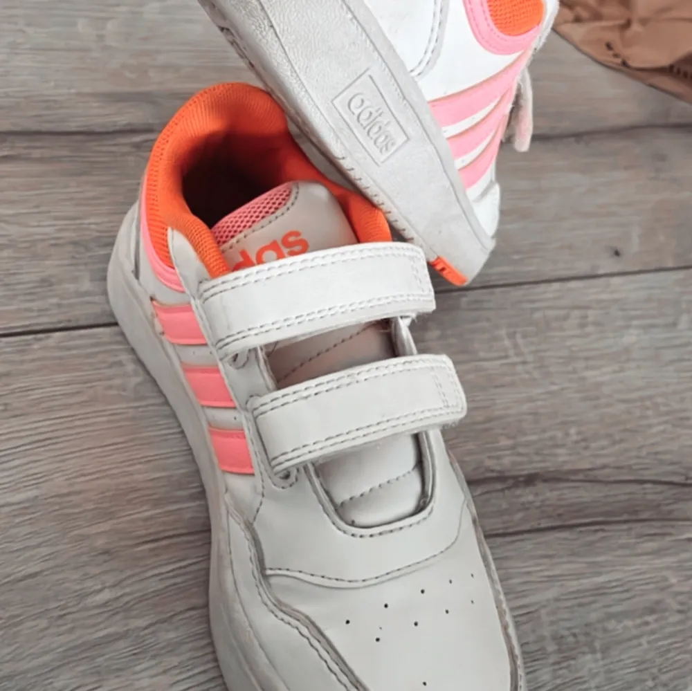 Snygga vita sneakers barn storlek från Adidas med rosa och orange detaljer. Skorna har kardborreband för enkel på- och avtagning och en bekväm passform. Knappt använda i st 31. Kengät.