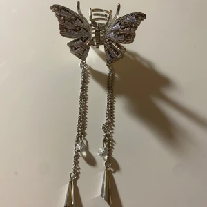 Hårklämma i fjärilsdesign - Elegant hårklämma i form av en fjäril med glittriga detaljer. Klämman är i silverfärg och har hängande kedjor med kristalliknande dekorationer. Perfekt för att ge en extra touch till din frisyr. Super söt att sätta i håret, den är liten och söt och perfekt till håret💗 priset går att diskutera🥰