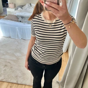 Randig kortärmad topp - Säljer en stilren randig topp i svart och beige. Den har korta ärmar och en rund halsringning. Perfekt för en avslappnad look.