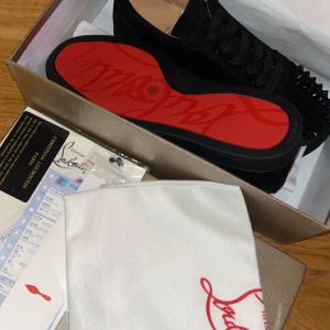 Svarta sneakers med nitar från Christian Louboutin - Sprillans nya snygga  svarta sneakers från Christian Louboutin med ikonisk röd sula och nitar på ovansidan. Skorna har snörning och är tillverkade i skinn, vilket ger en lyxig känsla. Perfekta för att ge en edgy touch till din outfit. Box, kvitton, box, kort, påse ingår! Hör av er vid frågor