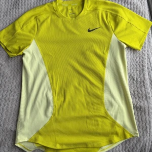 Gul kortärmad t-shirt från Nike - Säljer en sportig gul t-shirt från Nike med korta ärmar och en snygg svart logga på bröstet. Perfekt för träning eller en aktiv dag. Materialet är lätt och andas bra.