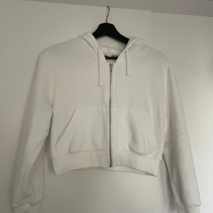 Vit croppad hoodie med dragkedja - Säljer en stilren vit croppad hoodie med dragkedja framtill. Den har en praktisk huva med dragsko och en stor ficka på magen. Perfekt för en avslappnad look. Från Shein.