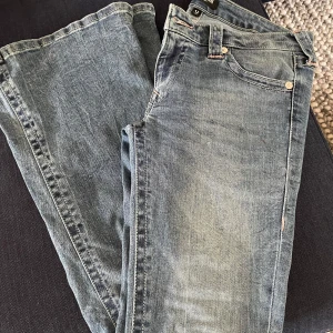 Blå jeans från True Religion - Säljer ett par snygga blå jeans från True Religion. De har en klassisk femficksdesign och ikonisk brodering på bakfickorna. Perfekta för en avslappnad stil.