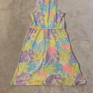 Färgglad ärmlös klänning med bladmönster - Säljer en somrig ärmlös klänning med ett färgglatt bladmönster i gult, lila, rosa och blått. Perfekt för varma dagar med sin lätta och luftiga design.