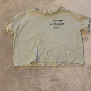 Beige t-shirt med tryck - Säljer en jus grön t-shirt med texten 'the sun is shining' tryckt på framsidan. T-shirten har en avslappnad passform och korta ärmar. Perfekt för en solig dag!