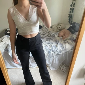 Vit spetslinne - Säljer ett snyggt vitt spetslinne med omlott-design och v-ringning. Toppen är ärmlös och croppad, perfekt för en stilren look. Den har en vacker spetsdetalj som ger en romantisk touch.