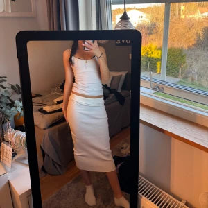 Vit ribbad kjol  - Säljer en stilren vit ribbad kjol med tight passform. Klänningen har en elegant midilängd som passar perfekt för sommarens alla tillfällen. Den har en enkel och klassisk design som gör den lätt att matcha med olika accessoarer.